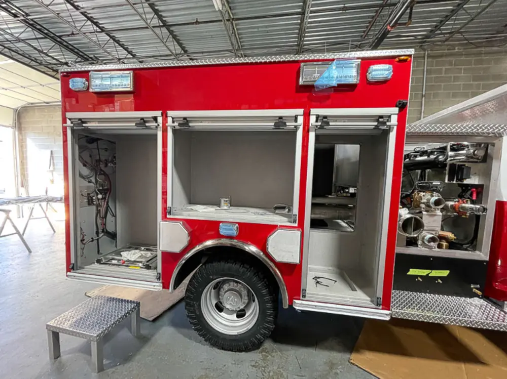Exterior view of small fire truck showing cab, body compartments, and wheel/tire area.